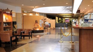 Un vestíbulo de hotel con mostrador de recepción, zona de estar y una escalera que lleva al piso superior.