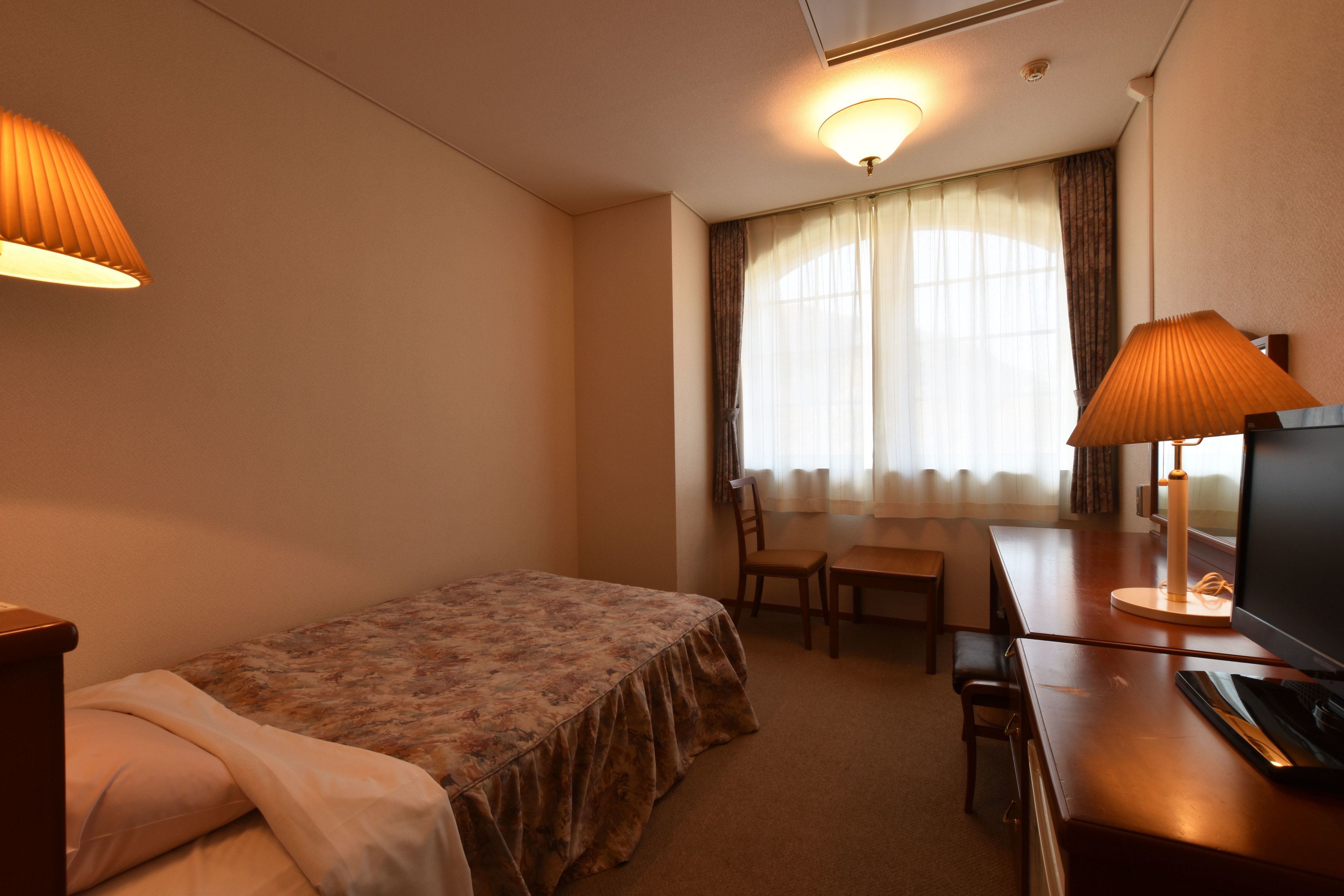 Una habitación de hotel con cama, escritorio con silla, televisión y ventana con cortinas.