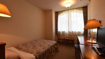 Una habitación de hotel con cama, escritorio con silla, televisión y ventana con cortinas.