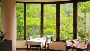 Comedor con una mesa dispuesta para dos personas, amplios ventanales con vistas a exuberante vegetación.