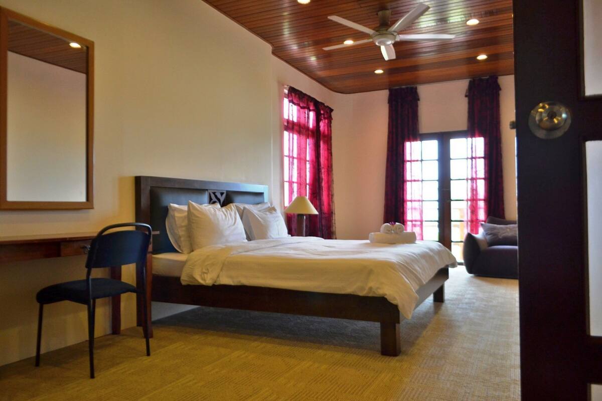 A bedroom with a bed, a chair, a ceiling fan, and a window with curtains.