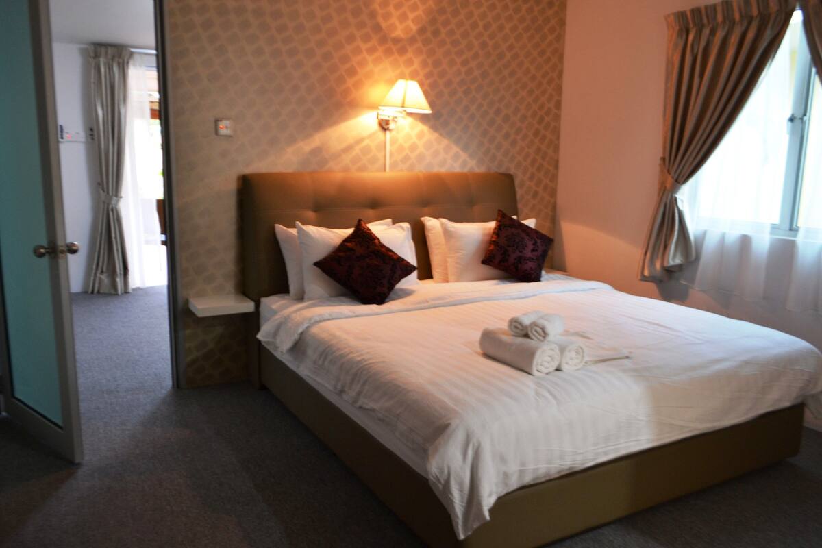 A neatly made bed with pillows and a rolled towel, a bedside lamp, and a patterned wall.