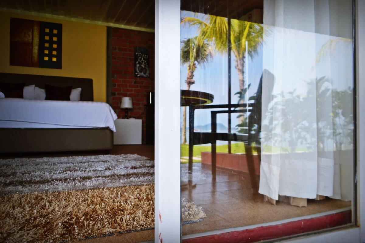 A room with a bed, a small table, and a view of a patio with palm trees.
