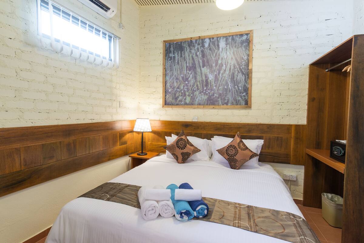 A hotel room with a wooden headboard, a large painting on the wall, a bed with white linens, and a nightstand with a lamp.