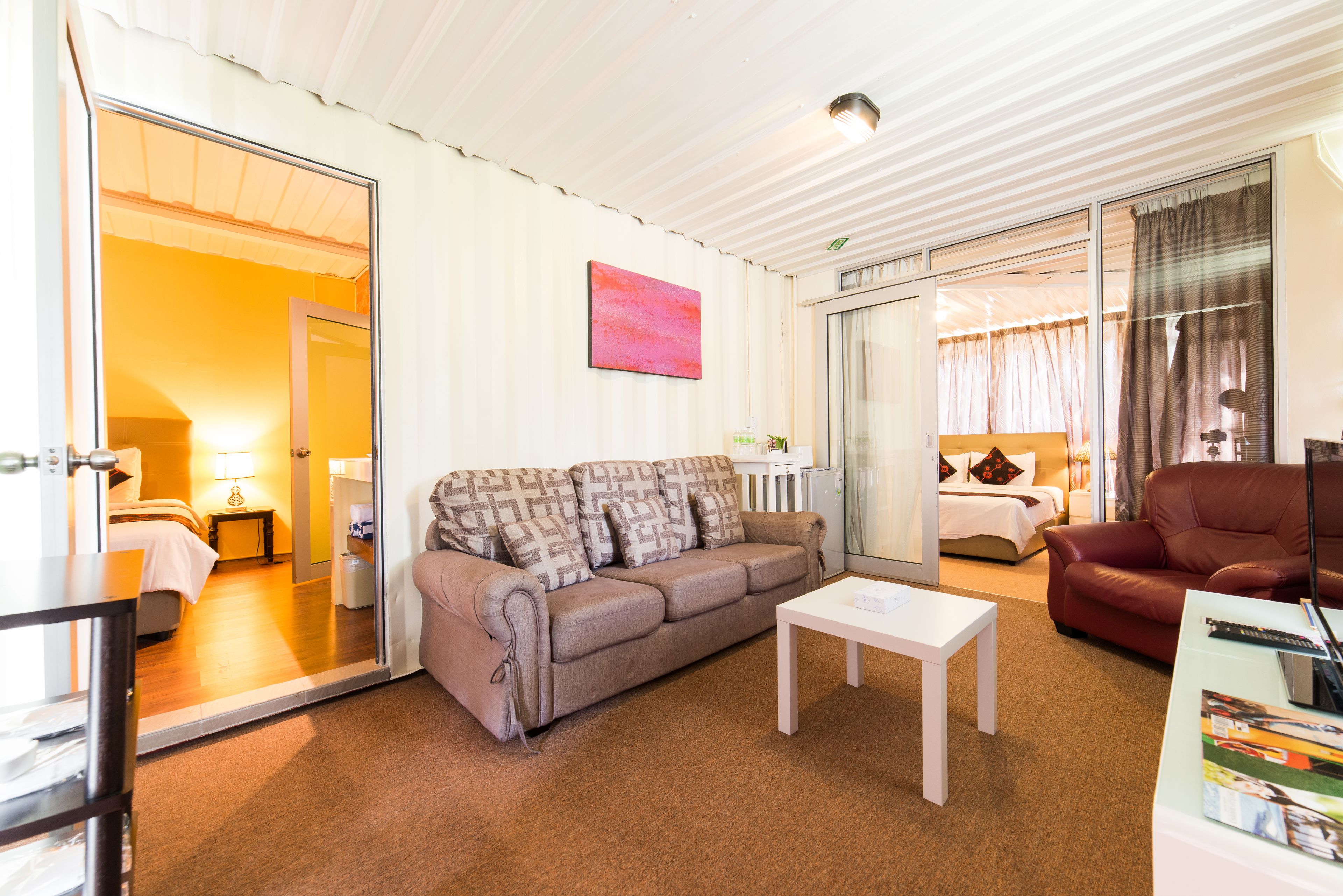 Ein modernes Hotelzimmer mit Sofa, einem kleinen Tisch, einem roten Sessel und einem Bett mit Nachtisch.