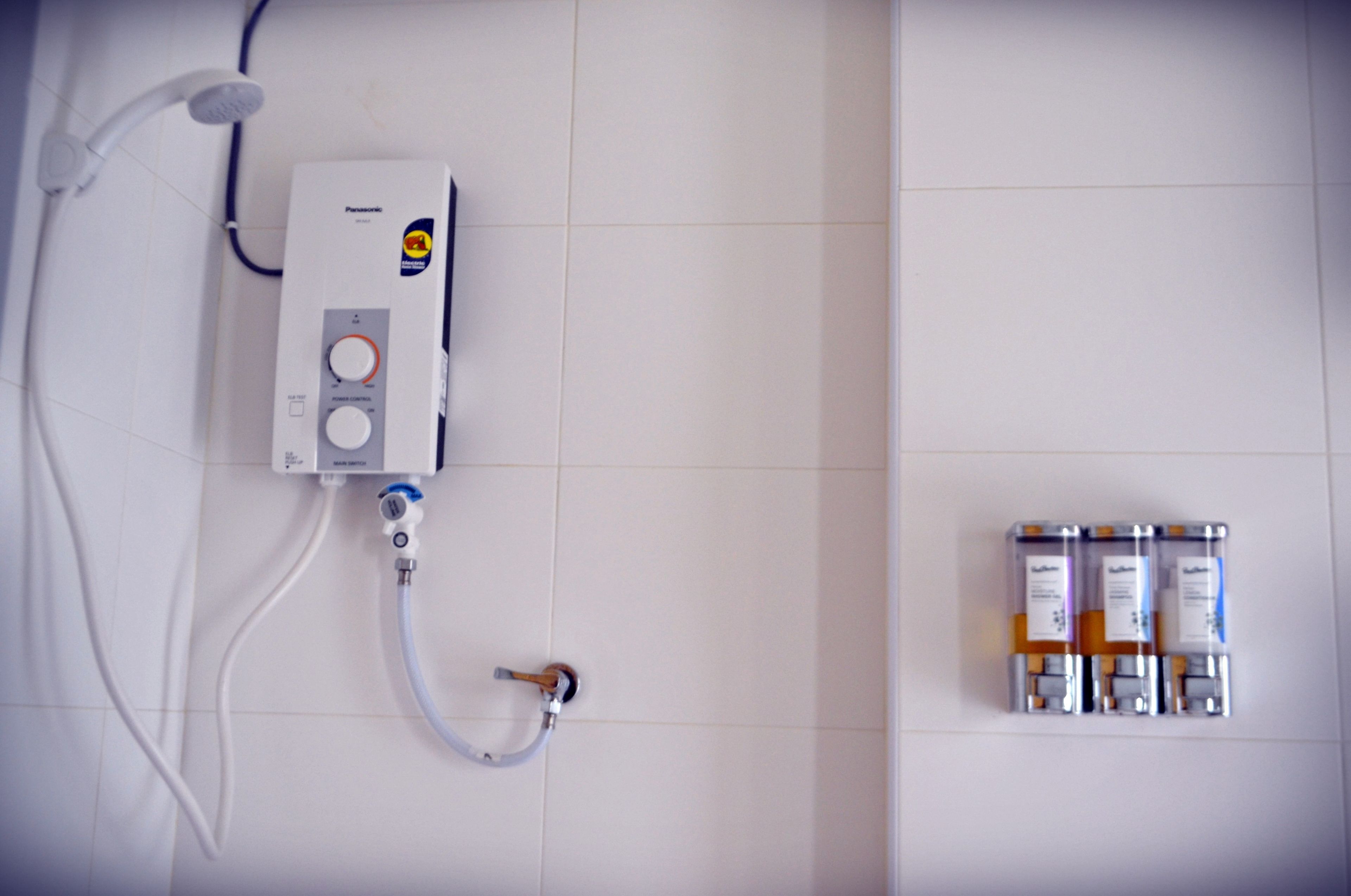Une salle de bain équipée d’un chauffe-eau, d’une douche et d’un ensemble de produits de toilette fixés au mur.