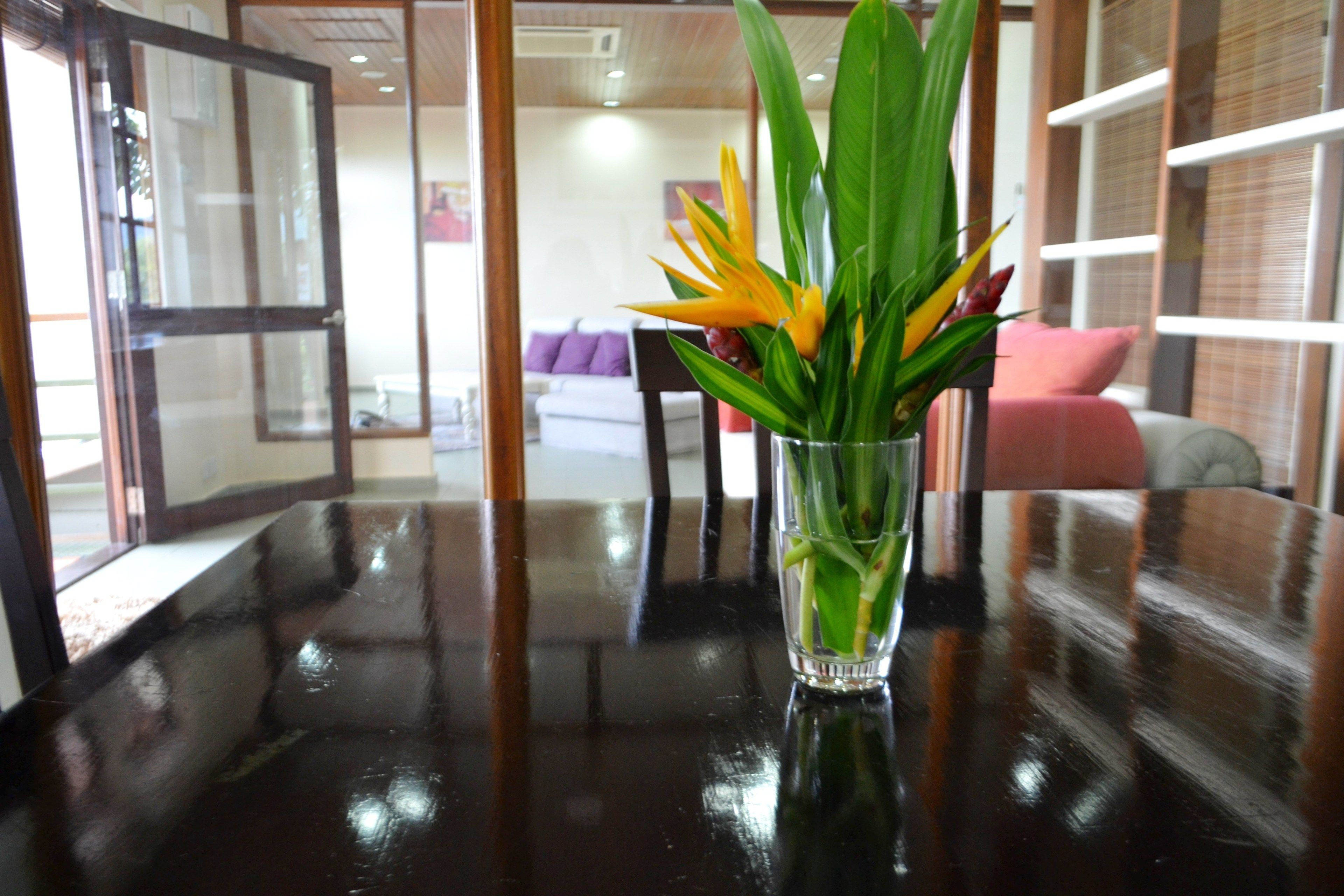 A glass vase with green leaves and a yellow flower on a reflective black table.