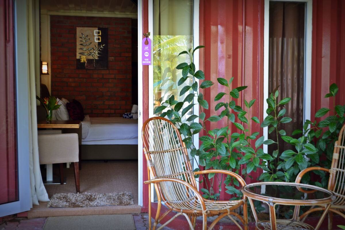 A room with a brick wall, a wooden chair, a glass table, and a potted plant.