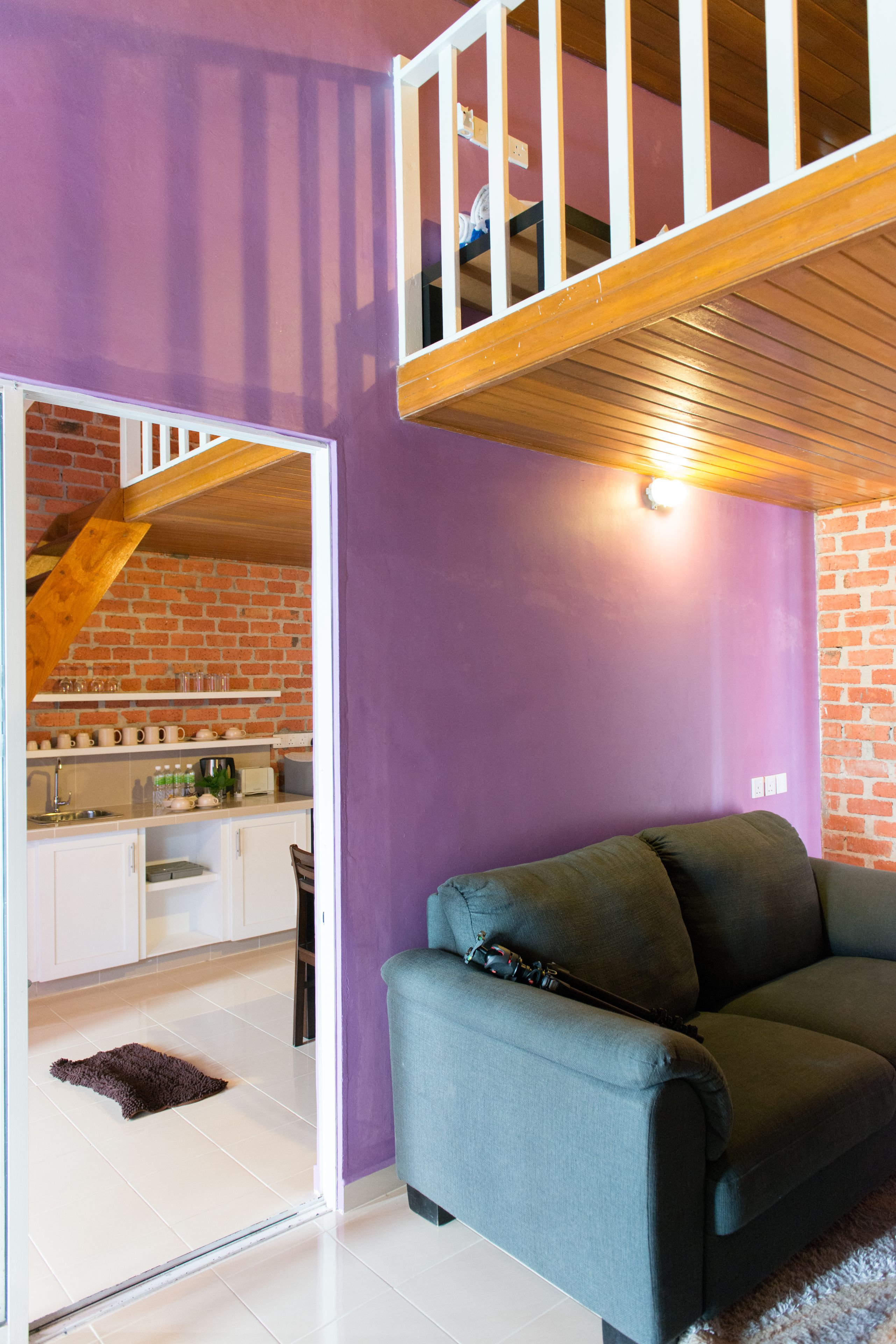 A room with a purple wall, a wooden staircase, a kitchen area with white cabinets, and a green sofa.