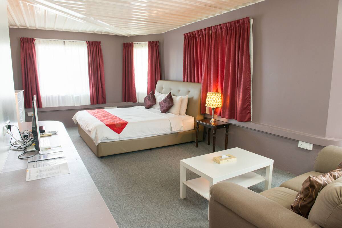 A hotel room with a bed, bedside table, and a desk with a computer and papers.