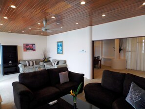 A modern living room with a wooden ceiling, a sofa set, a coffee table with a vase, and a television.