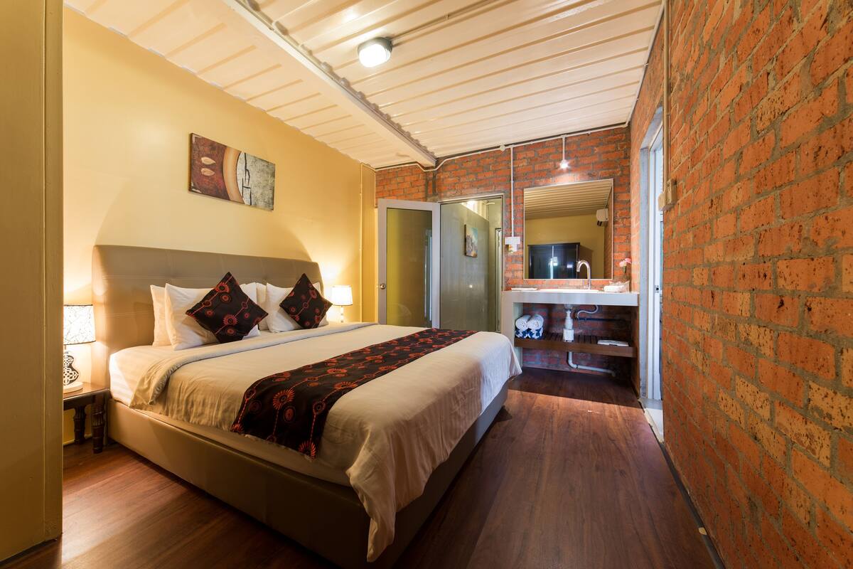 A bedroom with a bed, bedside table, lamp, and a brick wall.