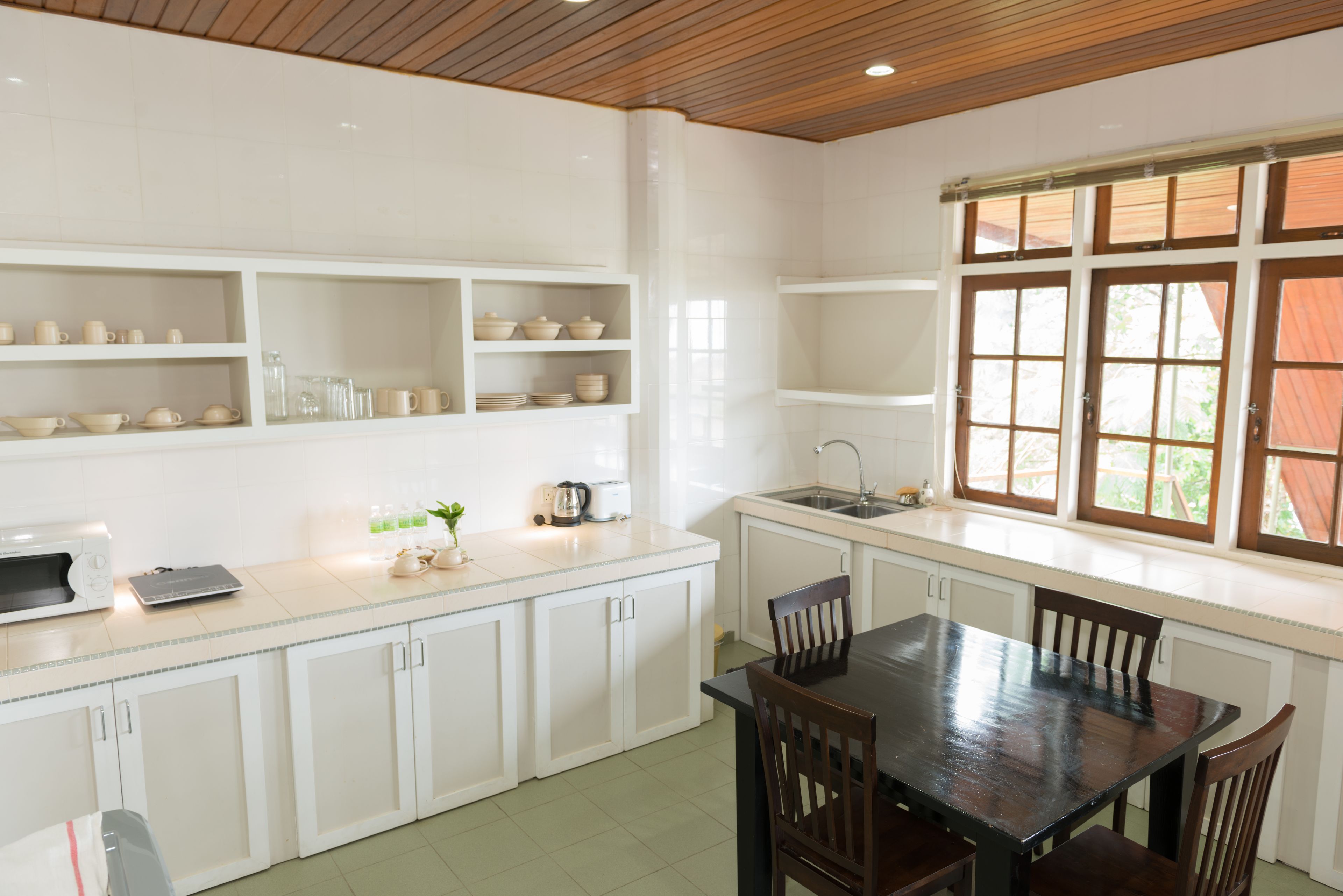 Une cuisine avec des meubles blancs, une table à manger en bois et une fenêtre à carreaux.