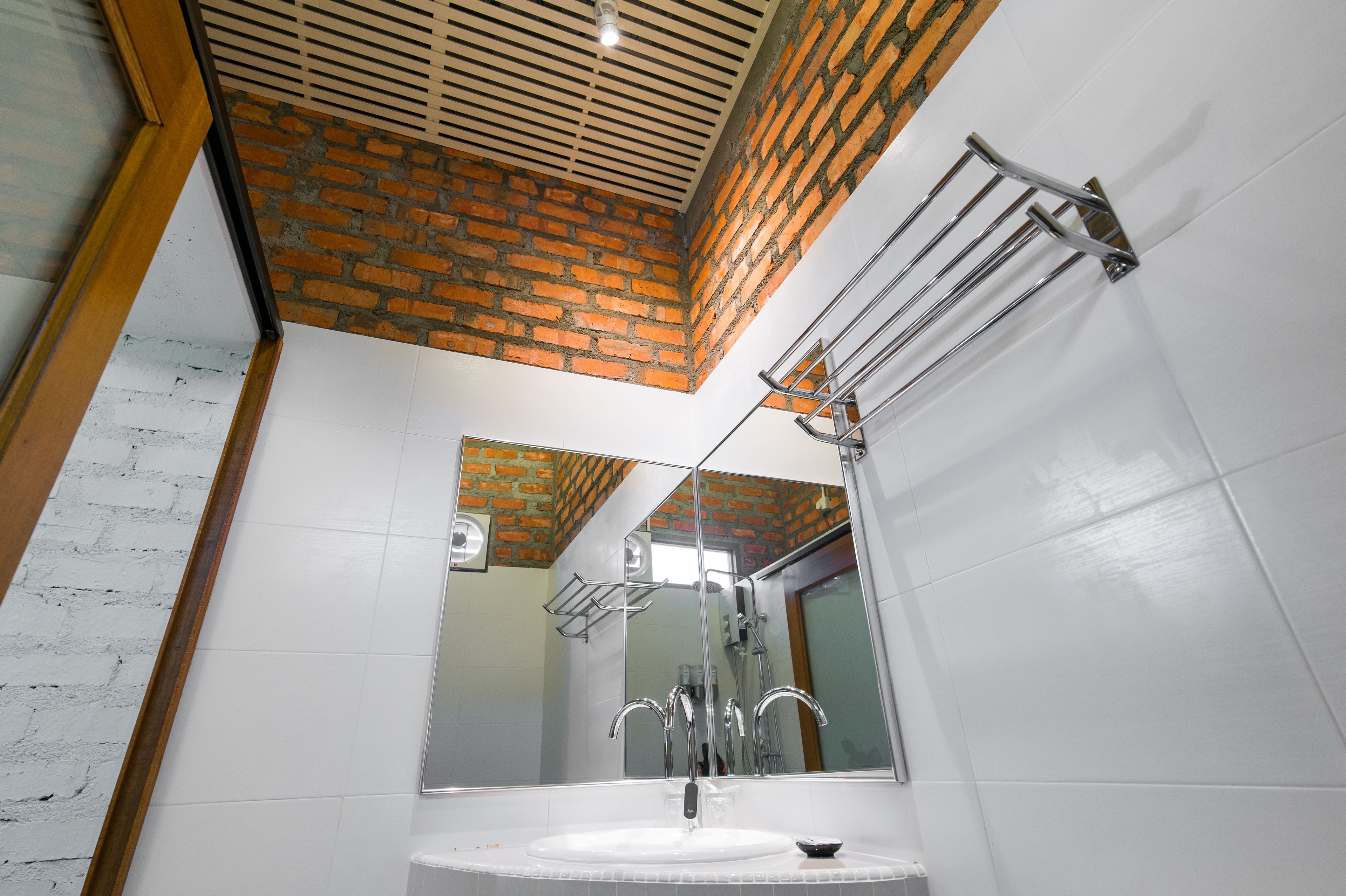 Une salle de bain avec un lavabo blanc, des robinets chromés, une douche en verre et un plafond orné d’un motif en briques.