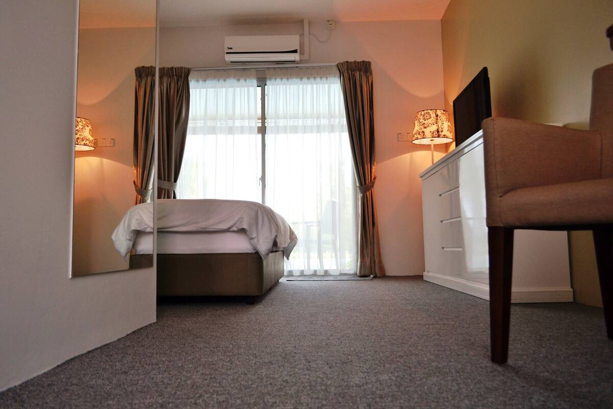 A hotel room with a bed, a chair, a desk, and a window with curtains.