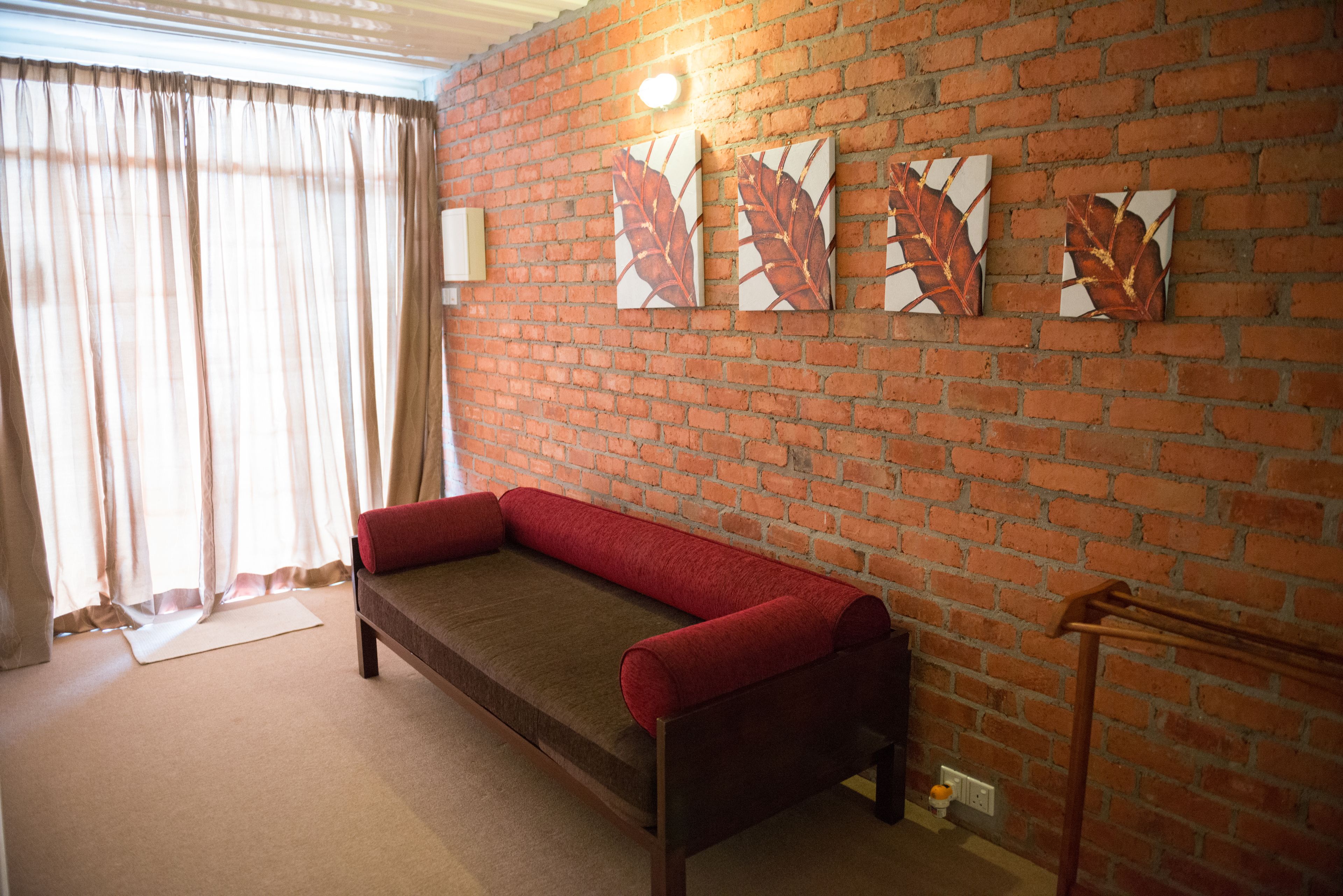 A room with a brick wall, a red sofa, and three leaf-patterned artworks.
