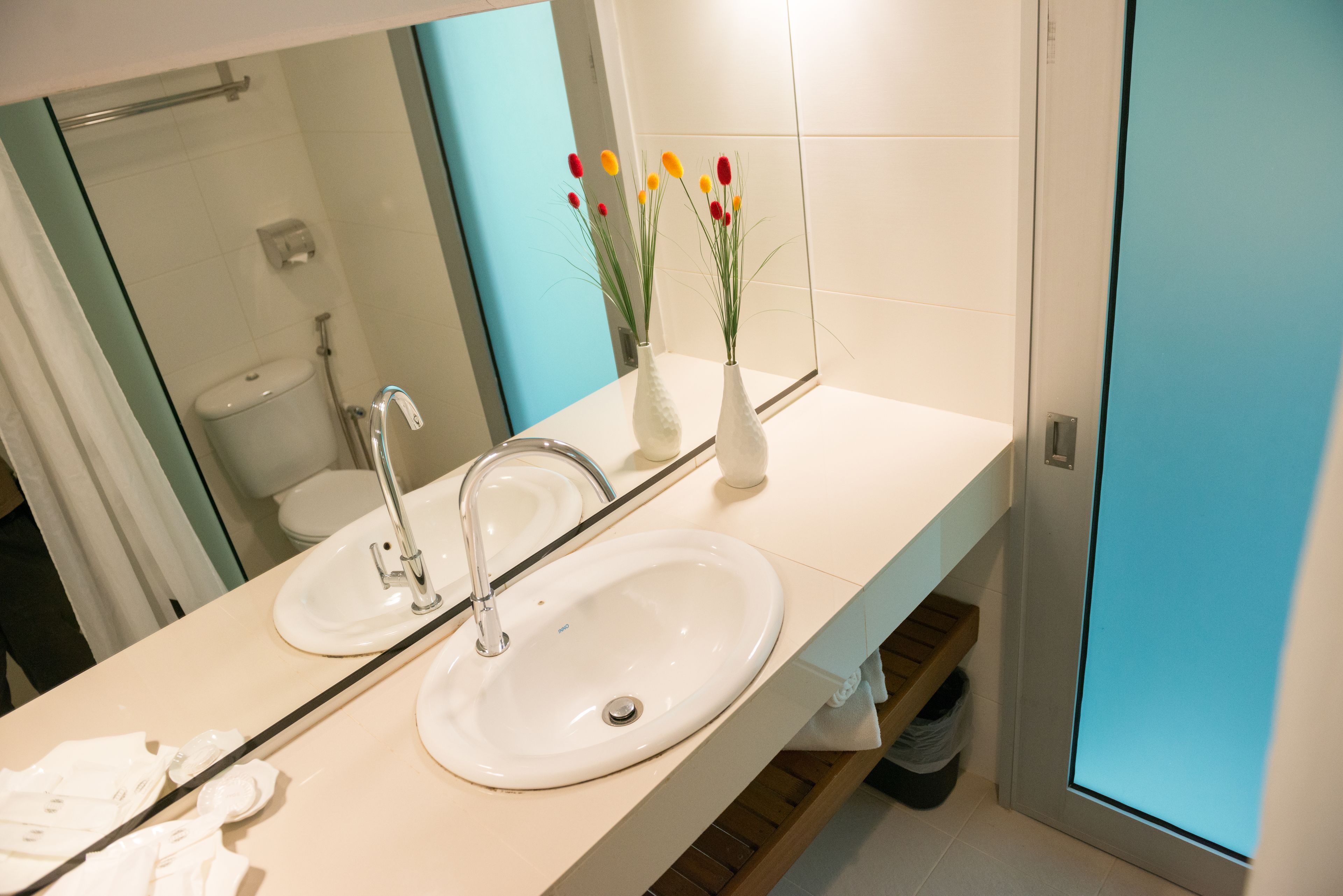 A bathroom with a white sink, a mirror, and a vase with flowers.