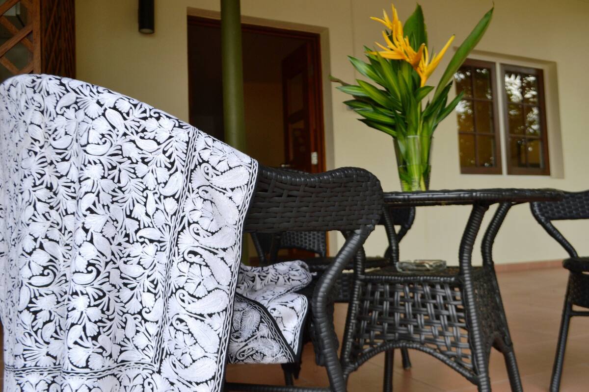 A wicker chair with a patterned cover, a table, and a vase with yellow flowers.