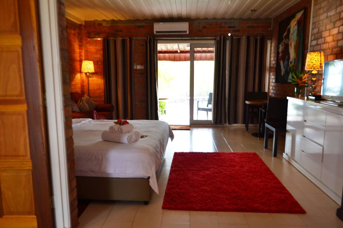 A hotel room with a bed, a red rug, a desk, and a chair.
