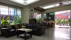 A spacious living room with a leather sofa, a coffee table, and a dining area with a table and chairs. There is a large window with a view of a fence and a building outside. - Airport Resident 2 (Chiang Mai)