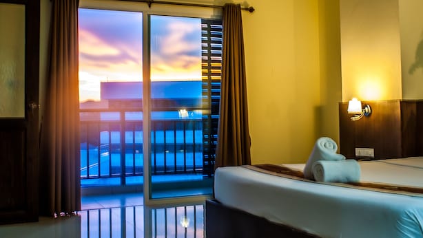 A hotel room with a bed, a nightstand, a lamp, and a view of the ocean at sunset. - Airport Resident 2 (Chiang Mai)