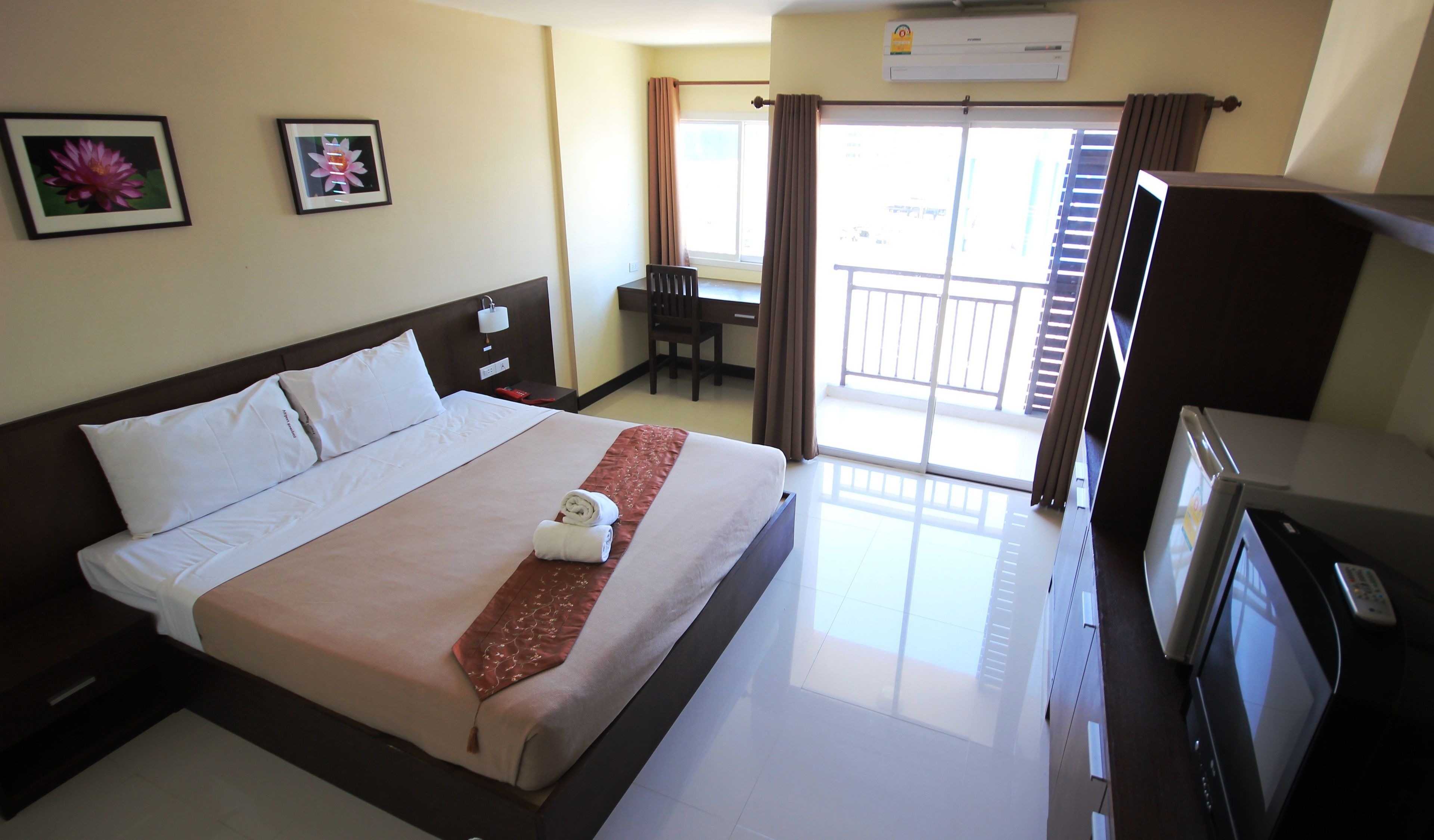 A hotel room with a bed, a desk, a chair, a TV, and a balcony with a view.