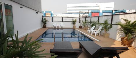 Una piscina con sillones de descanso y plantas en macetas.