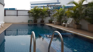 An indoor swimming pool with clear blue water, surrounded by potted plants and white chairs. - Airport Resident 2 (Chiang Mai)