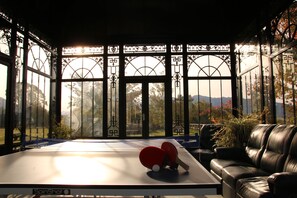 Une table de ping-pong avec deux raquettes, dans une pièce dotée d’une grande fenêtre, d’un canapé en cuir et d’une table de tennis de table de la marque SpinShot.