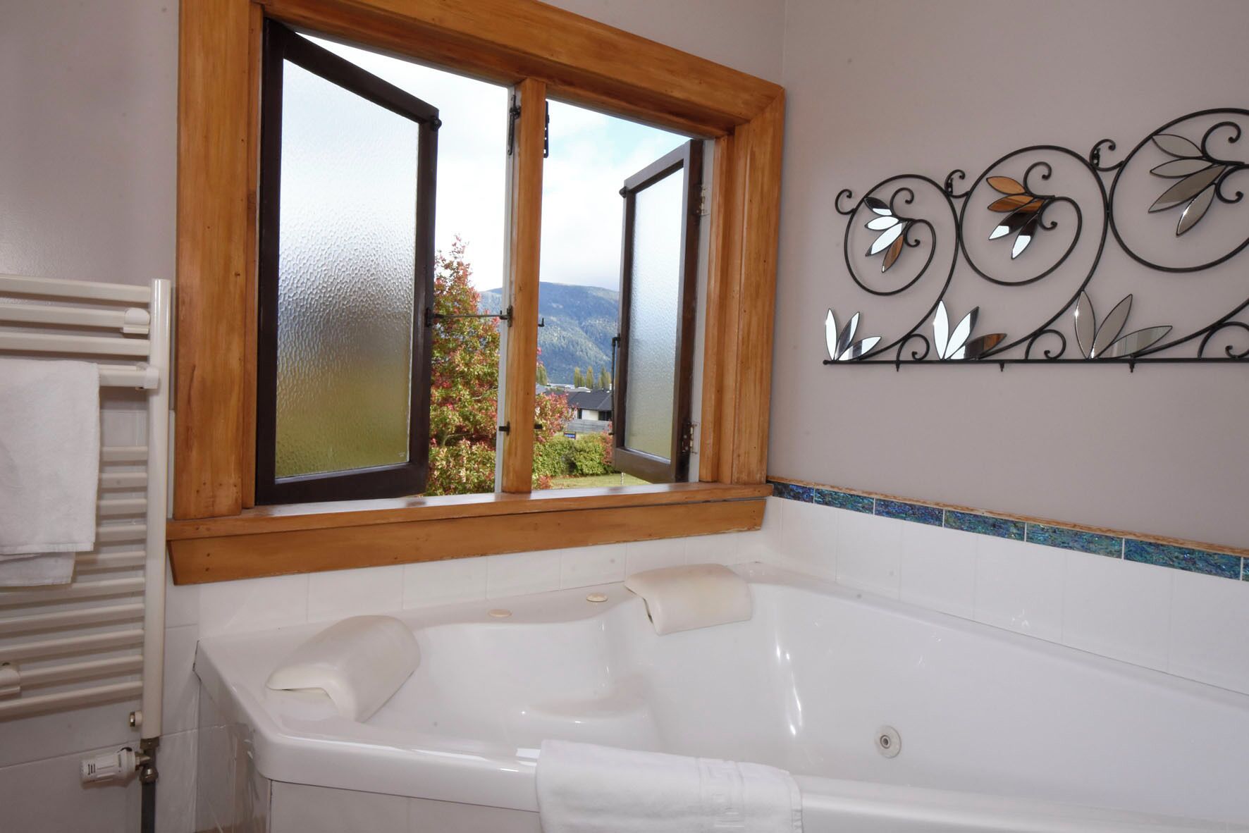 Ein Badezimmer mit einer großen Badewanne, einem Fenster mit satiniertem Glas und einem dekorativen Wandkunstwerk aus Metall.