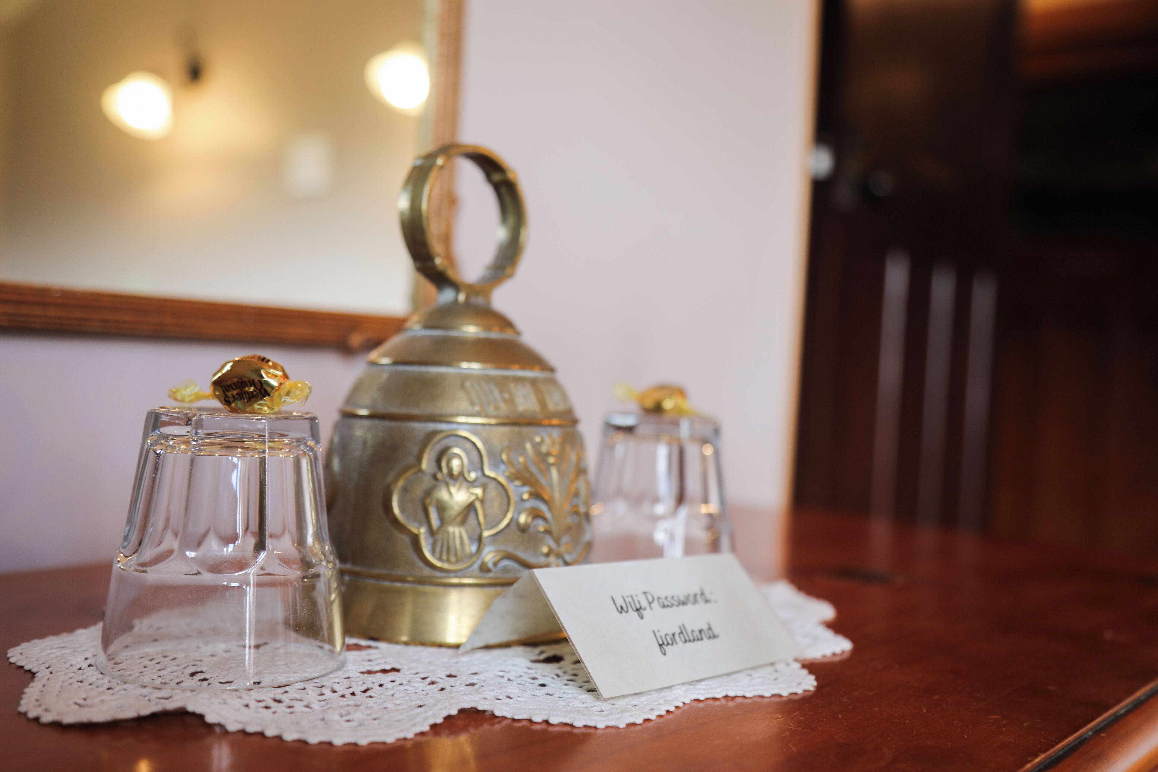 Una mesa con un recipiente de bronce, dos vasos de vidrio y una tarjeta con texto.