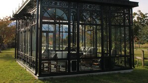 Um pavilhão com teto de vidro e grades de metal, localizado em uma área gramada.