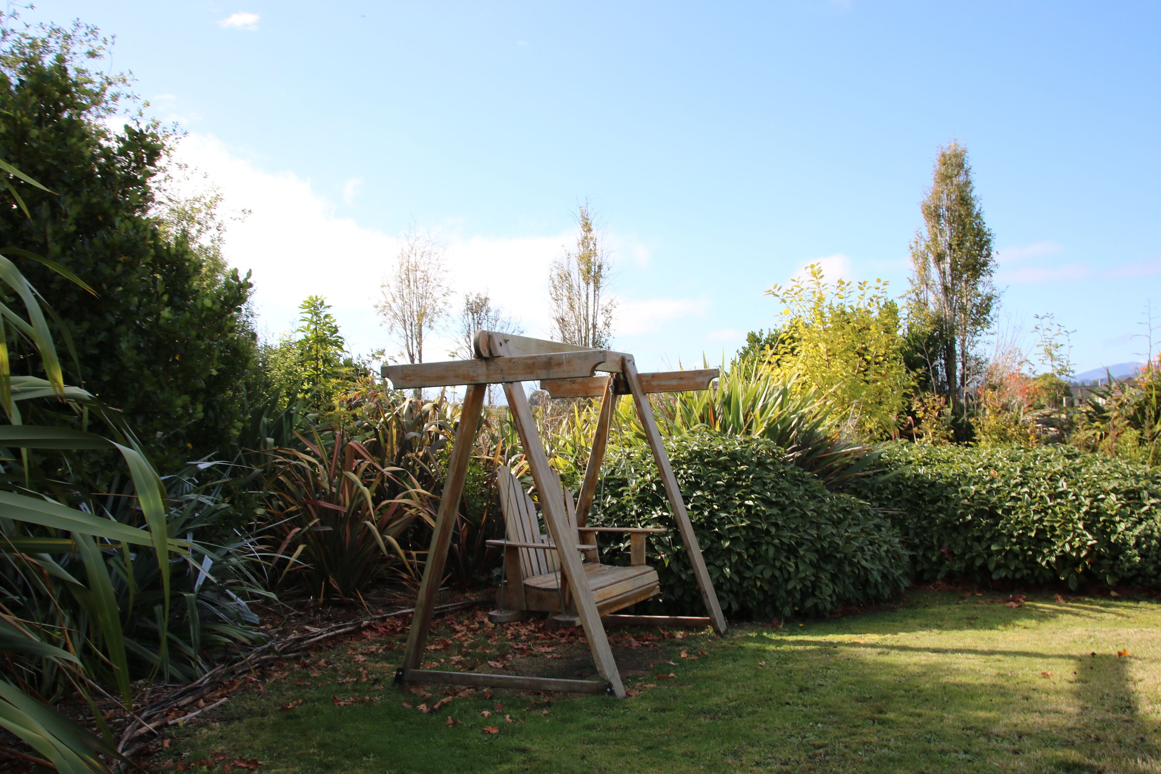 Un ensemble de balançoires en bois installé dans un jardin, avec une végétation luxuriante et des arbres en arrière-plan.