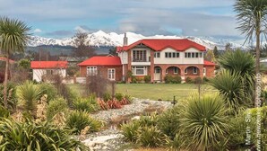 Uma casa grande com telhado vermelho, rodeada por um jardim bem cuidado e um pequeno lago.