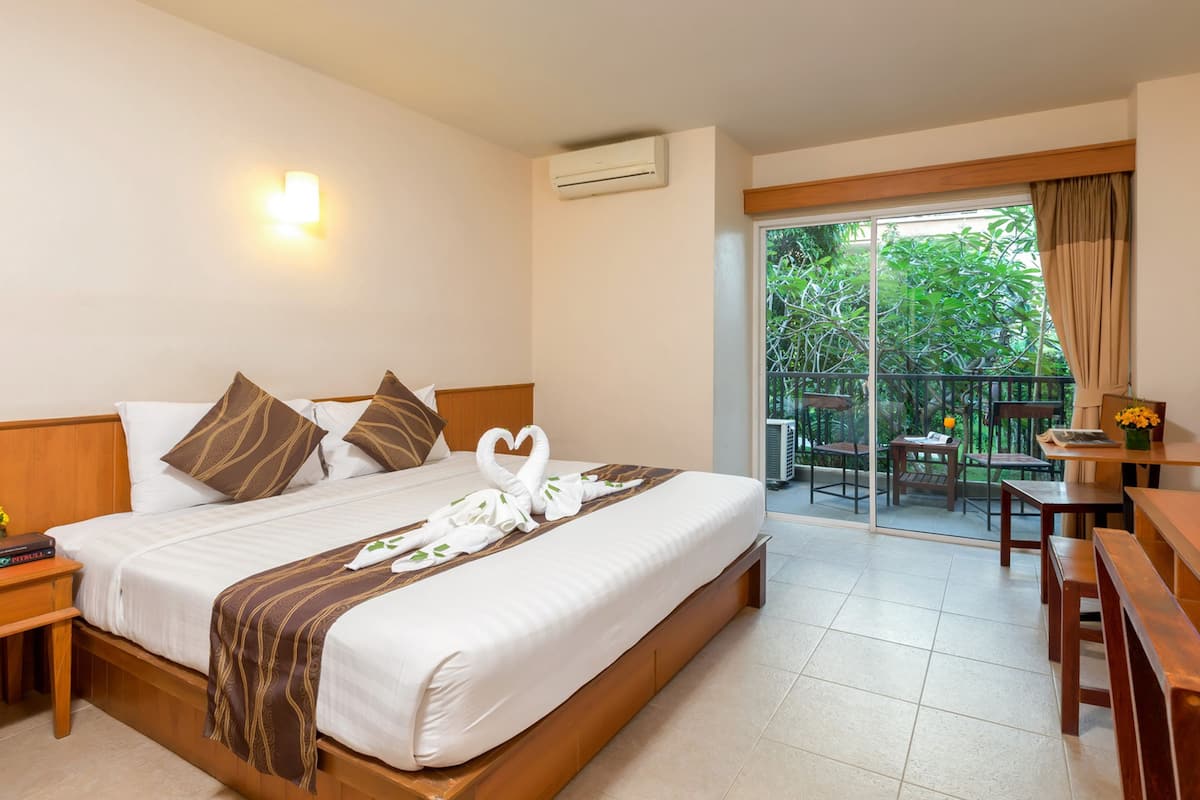 A hotel room with a large bed, a nightstand, a desk, and a balcony with a table and chairs.