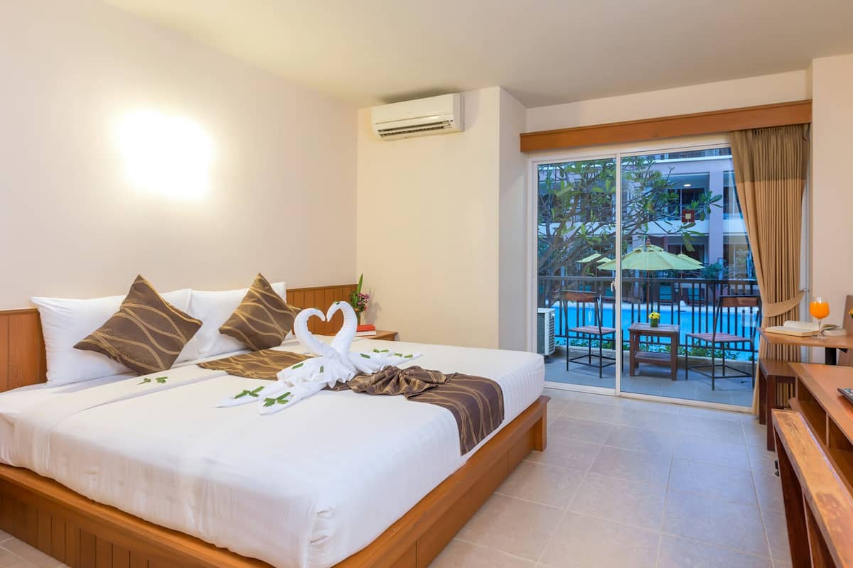 A hotel room with a bed, a nightstand, a desk, and a balcony with a pool.
