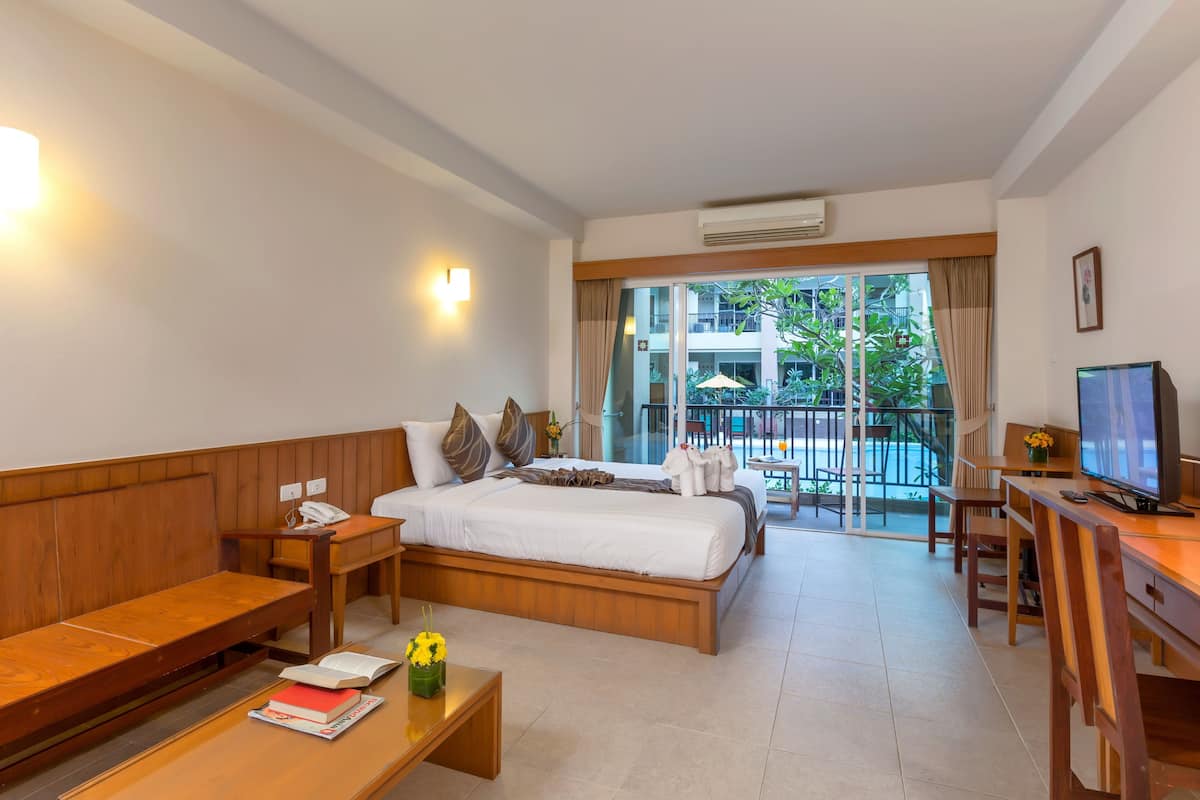 A hotel room with a bed, wooden bench, desk, and a TV.
