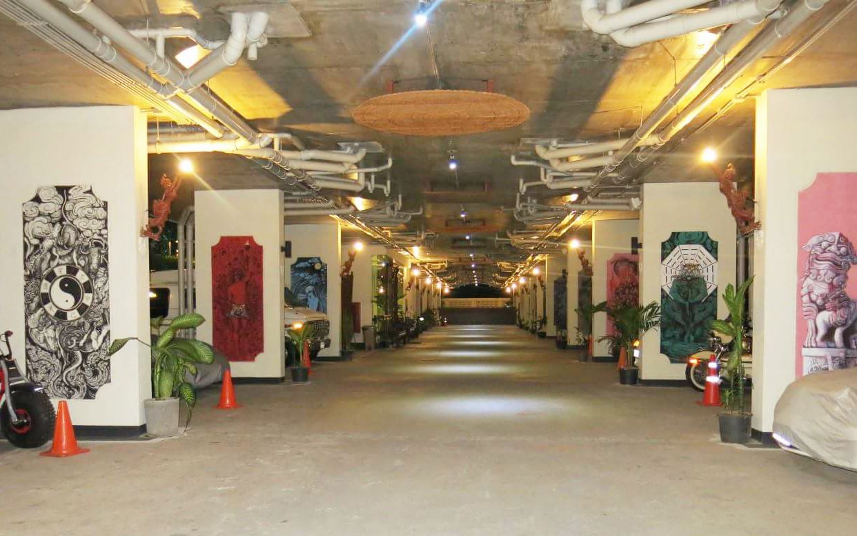 A hallway with artwork on the walls, potted plants, and a ceiling with exposed pipes.