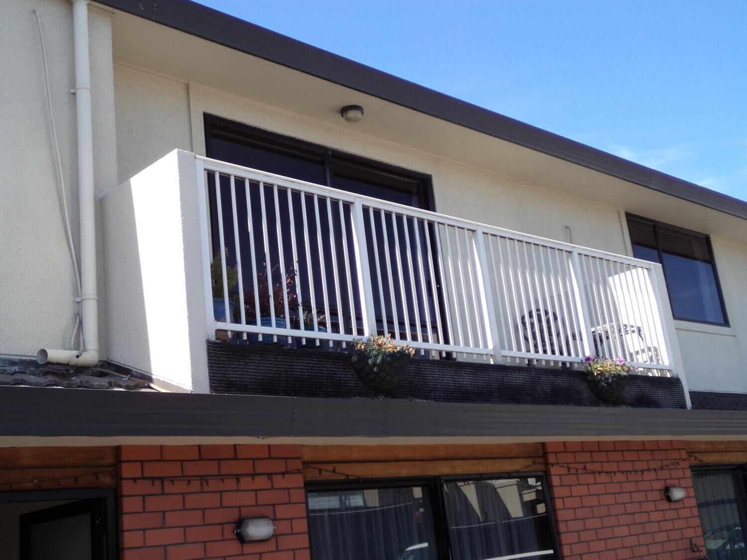 A two-story building with a balcony on the second floor, featuring a white railing and potted plants.