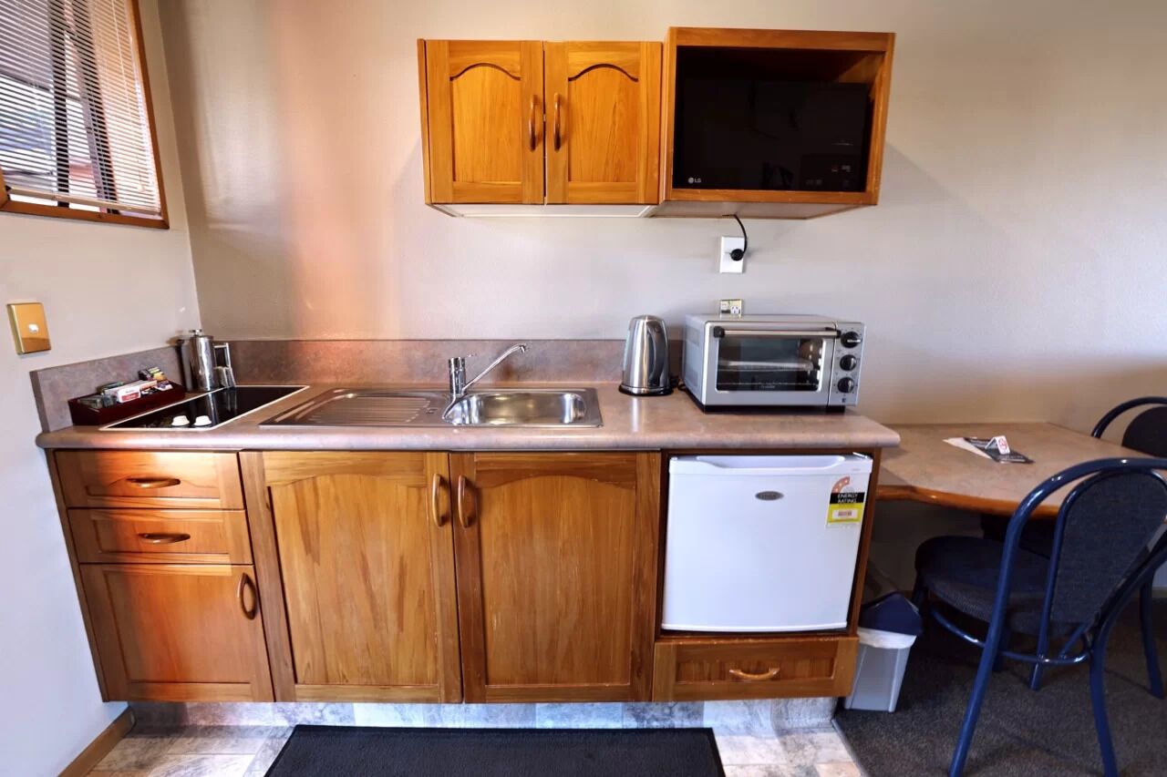 A compact kitchenette with wooden cabinets, a sink, a toaster, and a small refrigerator.