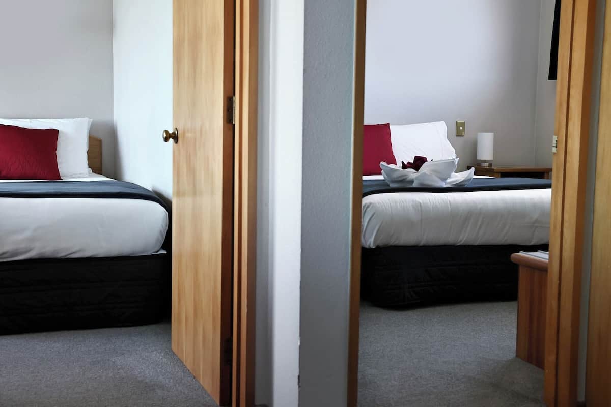 Ein Hotelzimmer mit zwei Betten, einer Holztür, einem Nachttisch und einer Lampe.