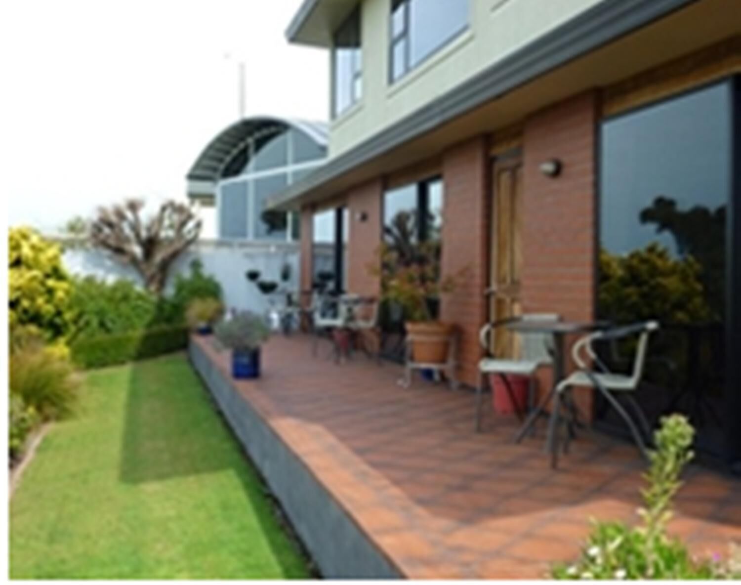 Een gebouw met een overdekte patio, terrasmeubels buiten en een verzorgde tuin.