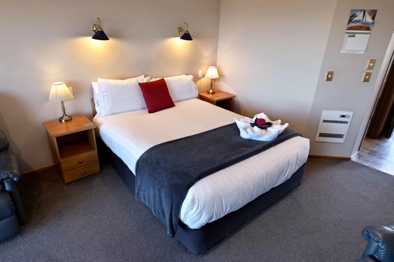 A neatly made bed with white and black bedding, two bedside lamps, and a red pillow.