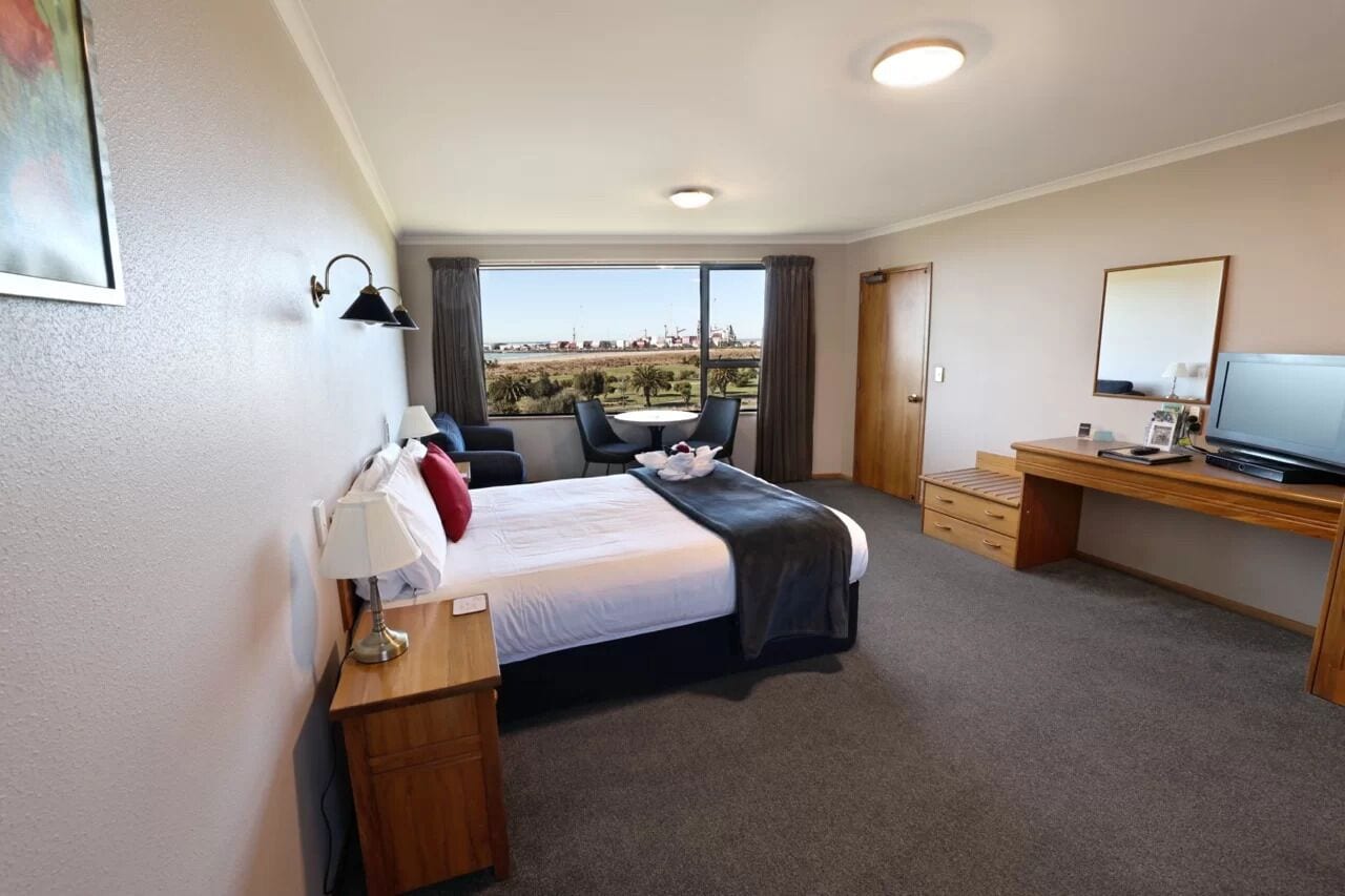 Habitación de hotel con cama, escritorio, televisor y vistas al exterior.