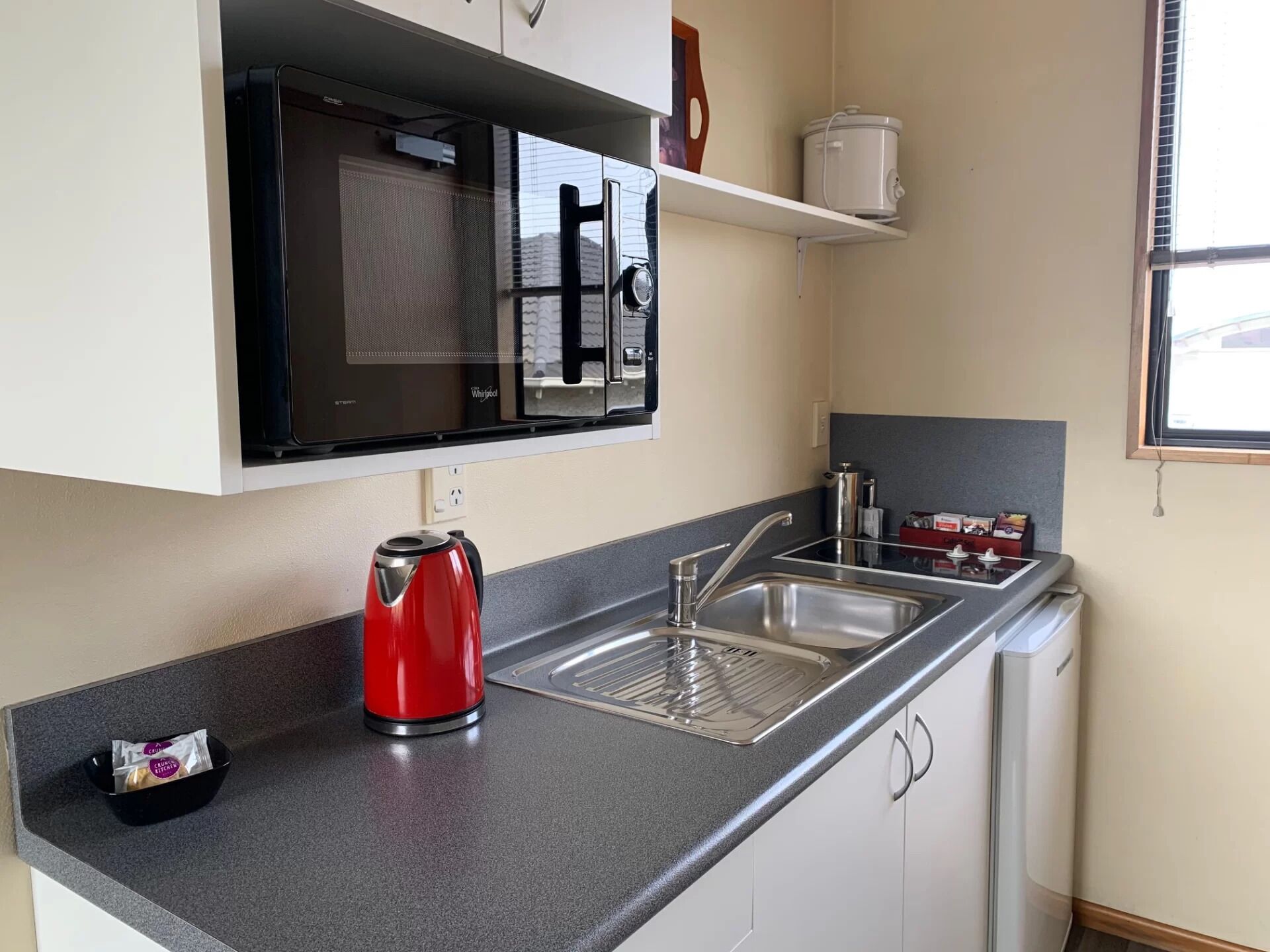 Een kleine keuken met een ingebouwde magnetron, een waterkoker en een spoelbak.