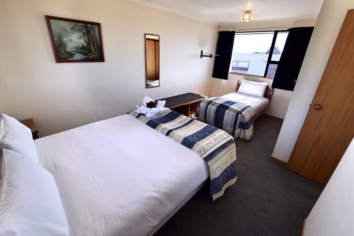 Ein Hotelzimmer mit zwei Betten, einem Bild an der Wand, einem Spiegel und einem Fenster mit Vorhängen.
