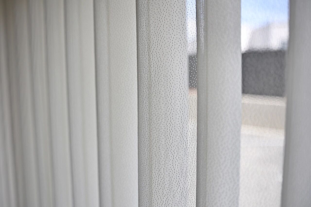 A close-up of a window with white blinds partially drawn, allowing a glimpse of the outside.