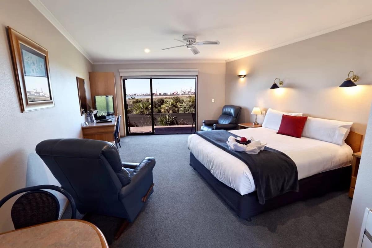 Ein Hotelzimmer mit einem Bett, einem Schreibtisch mit Computer, einem Stuhl und Blick ins Freie.