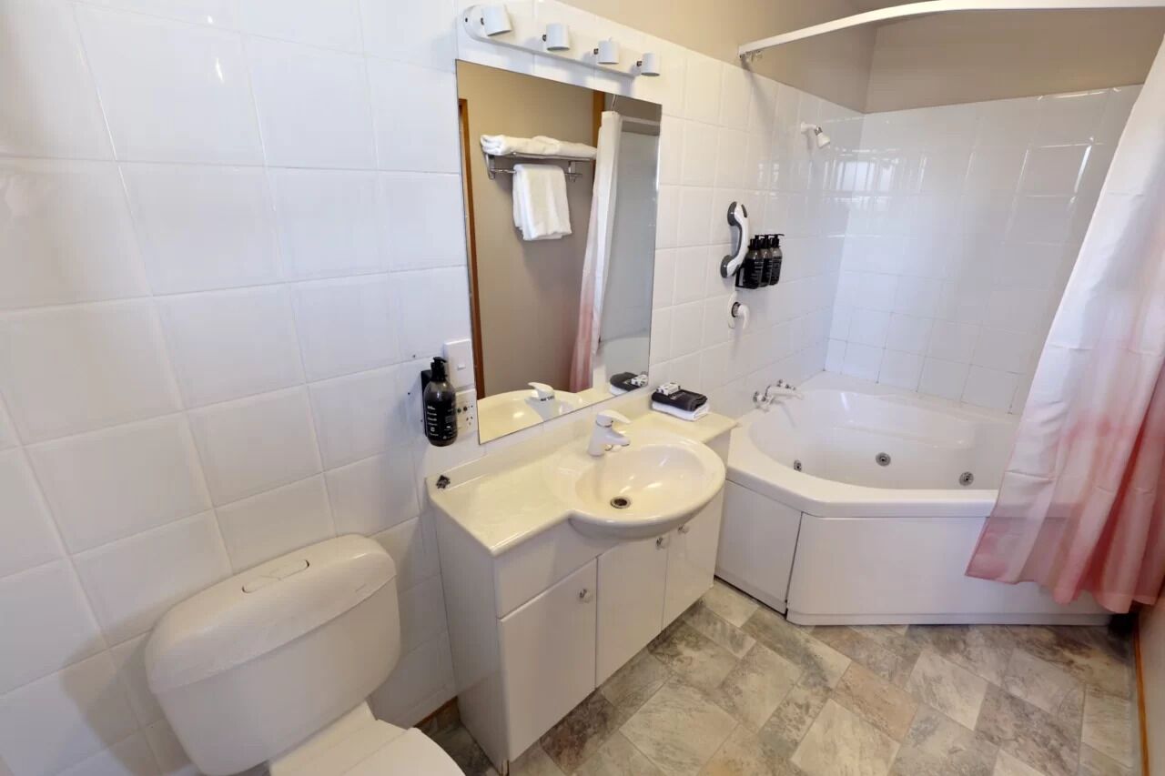 A bathroom with a toilet, sink, mirror, and a bathtub.