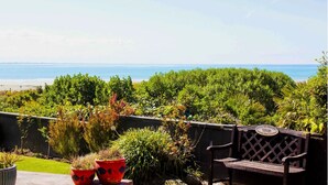 Une terrasse avec un banc et des plantes en pot, donnant sur une plage et l’océan.